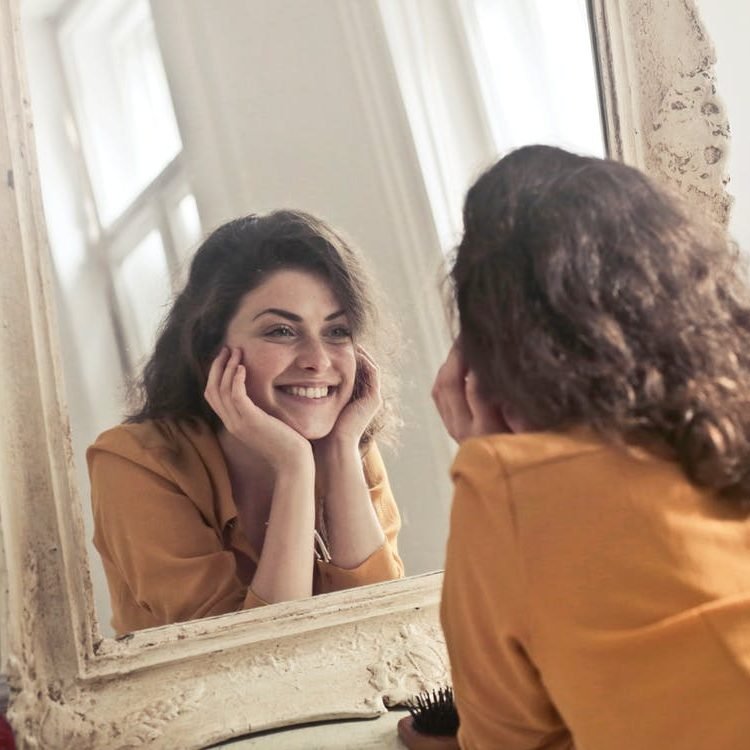 امرأة مبتسمة تنظر إلى انعكاسها في المرآة